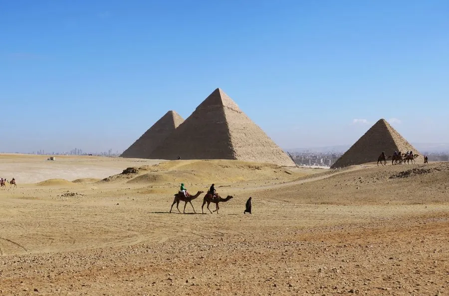 Camel riders passing the pyramids of Giza