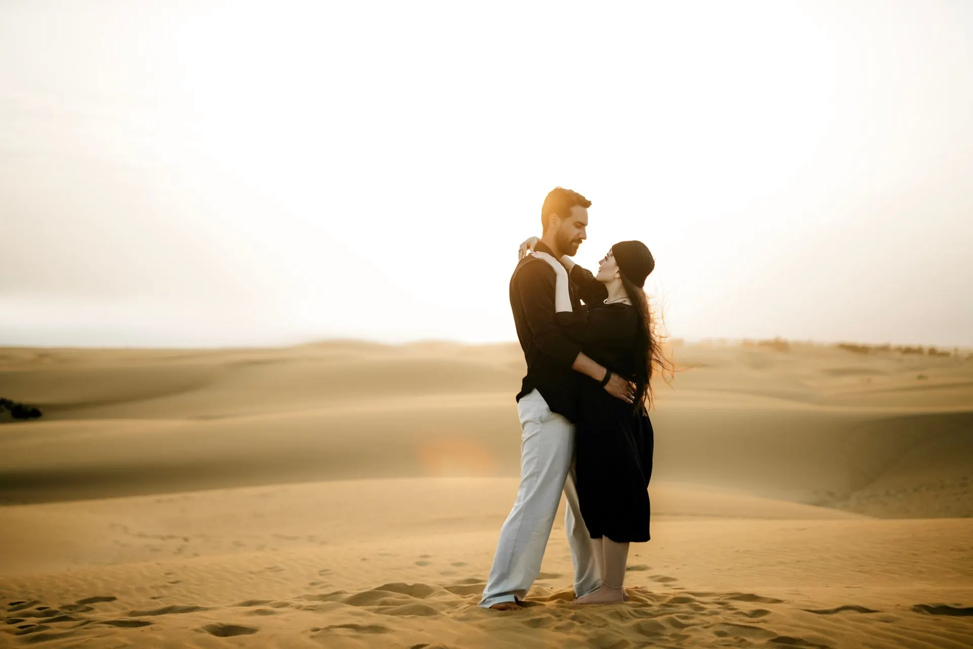 Couple embracing on desert dunes at sunset