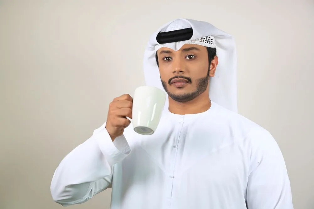 Travel agent in a white kandura and ghutra holding a cup of coffee