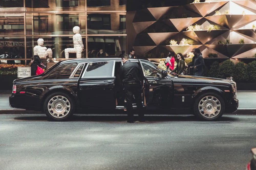 Chauffeur standing beside a black luxury saloon outside a boutique