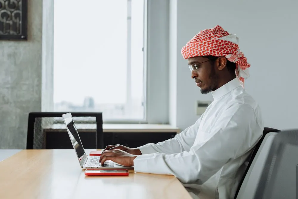 Consultant in a white thobe working on a laptop at a bright office desk