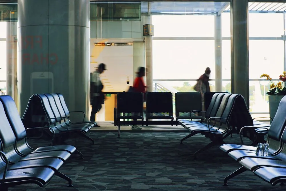 Travellers waiting in a bright airport lounge beside tall windows