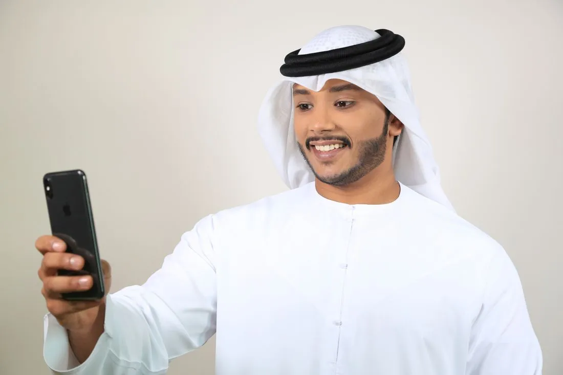 Smiling man in a white kandura and ghutra holding a smartphone