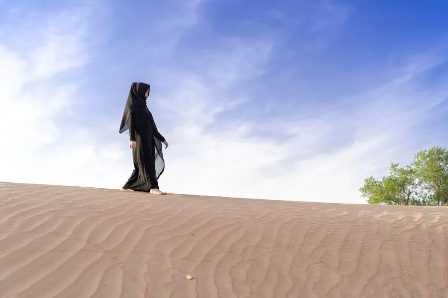 Woman in an abaya walking along the crest of a sand dune