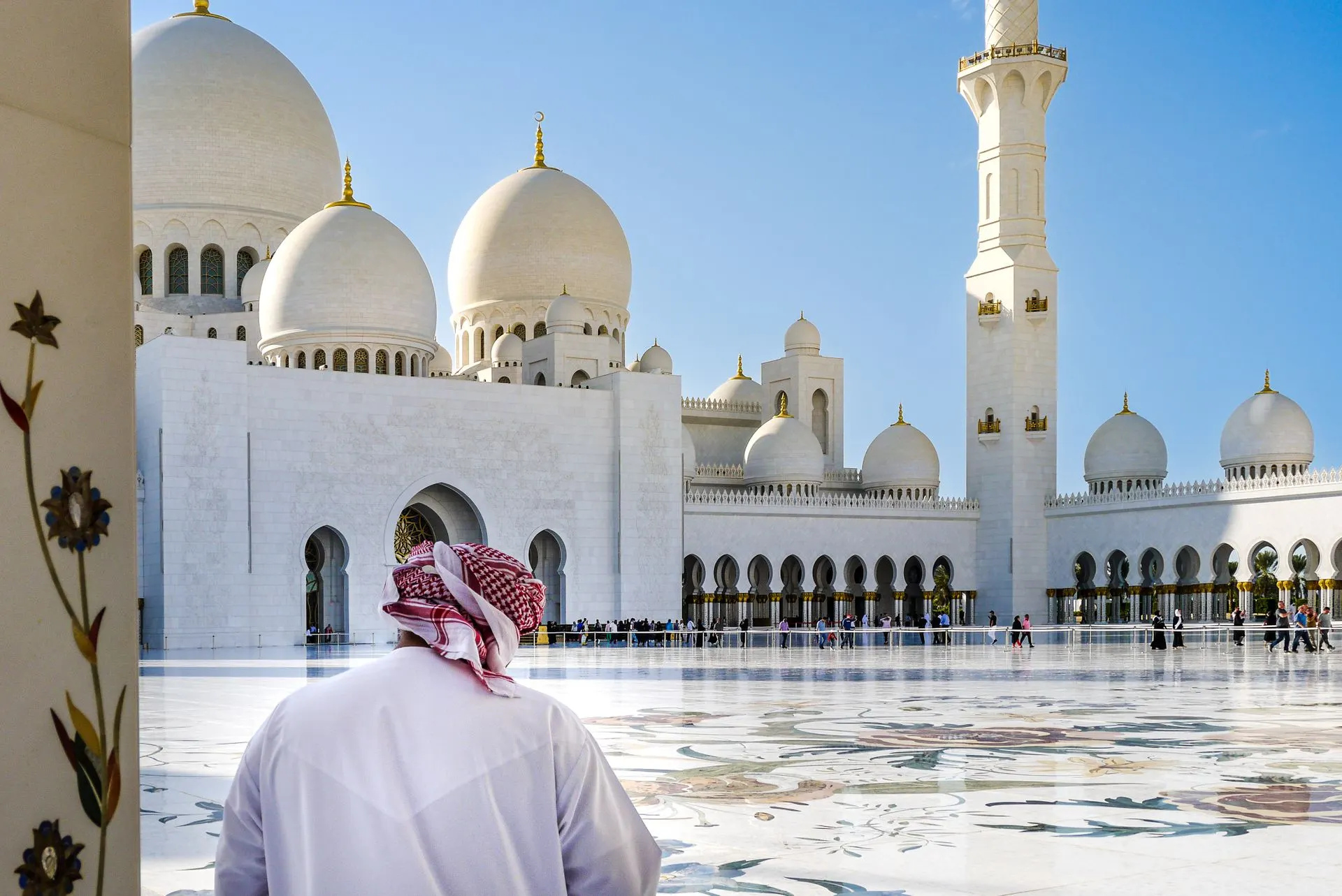 Man in a white kandura facing the domes of Sheikh Zayed Grand Mosque