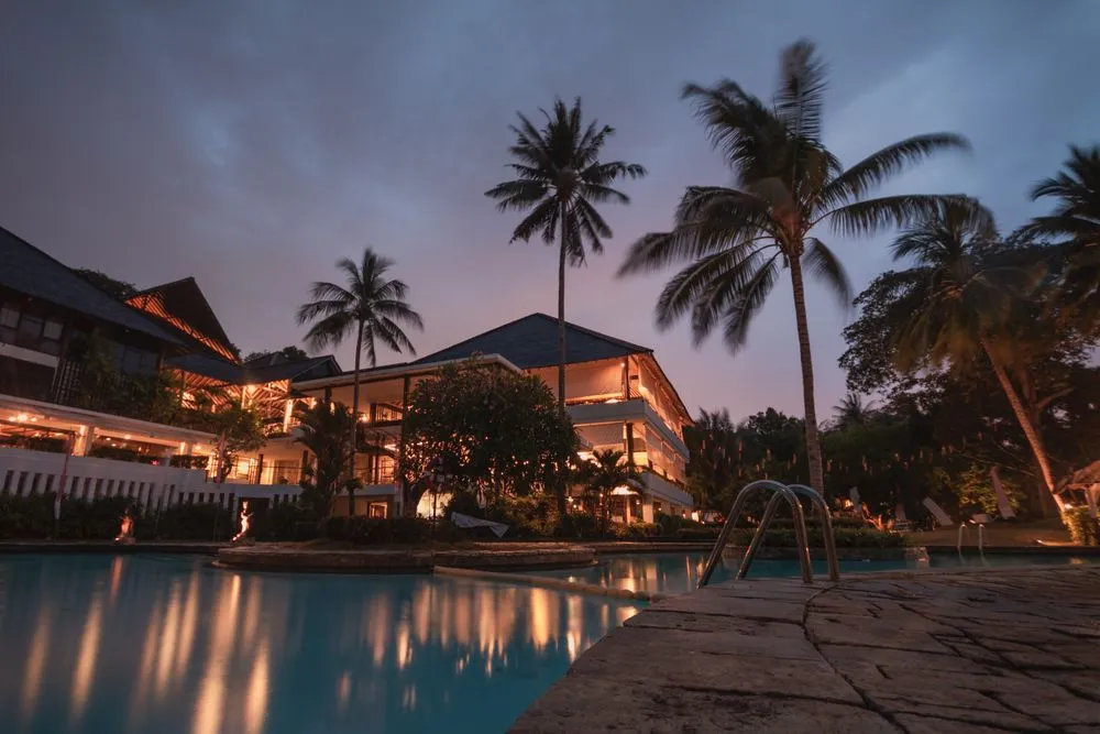Resort pool lined with palm trees at sunset